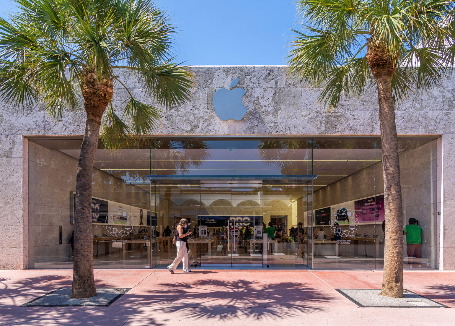 Outdoor café seating under fringed umbrellas beside a row of potted palm trees