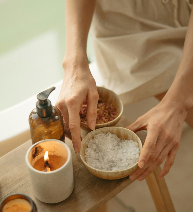 Hands arranging bath salts, a candle, & a pump bottle